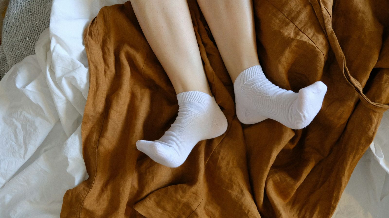 Feet in soft white socks resting on a bed with a rust coloured throw